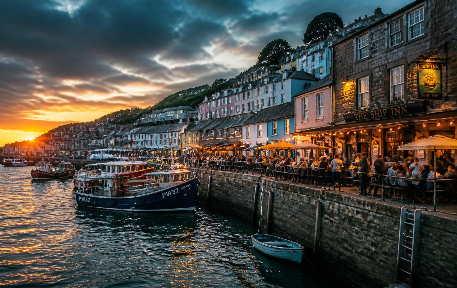 Cornish harbour at golden hour with a busy quayside pub terrace